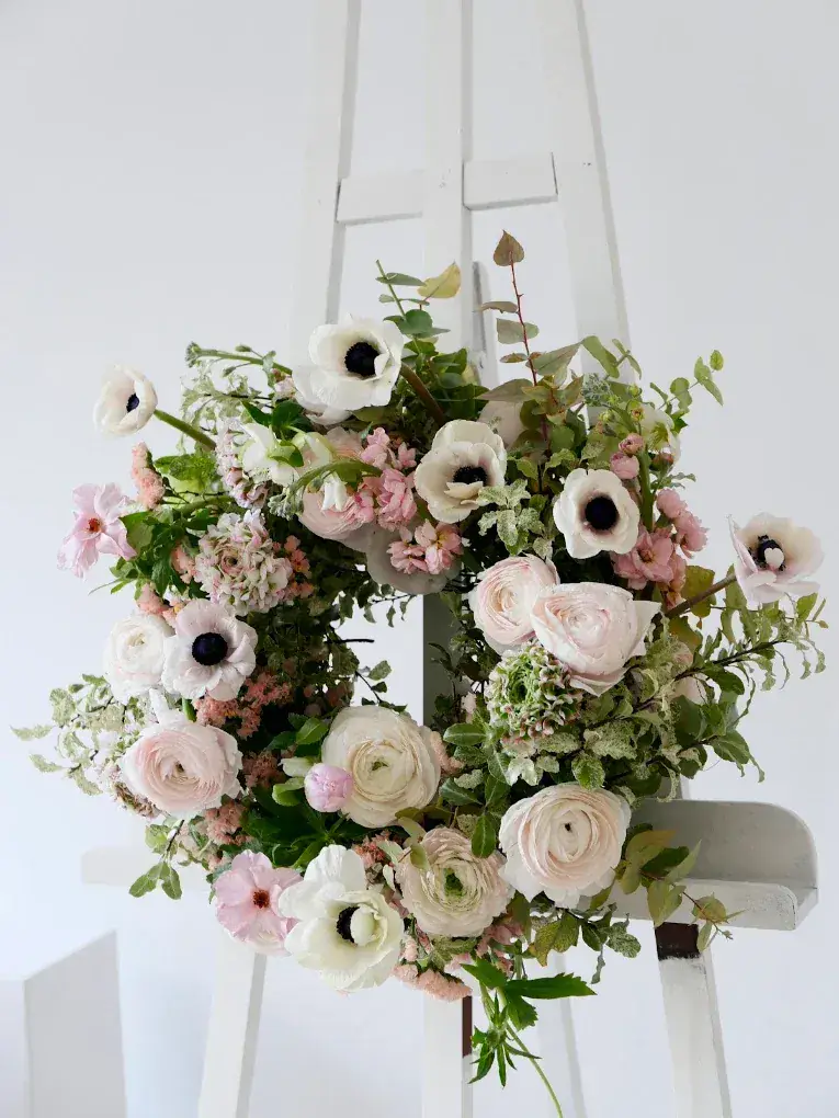 Couronne de deuil en anémones blanches, renoncules et roses roses, présentée sur un chevalet