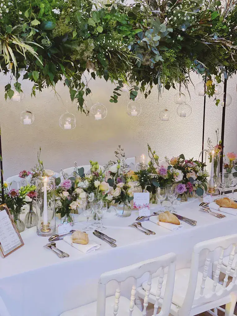Longue table de mariage sous une suspension végétale, chemin de fleurs pastel et bougies